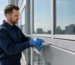 Technician in gloves cleaning a cured silicone sealant joint along an aluminium curtain wall mullion with a brush and cloth