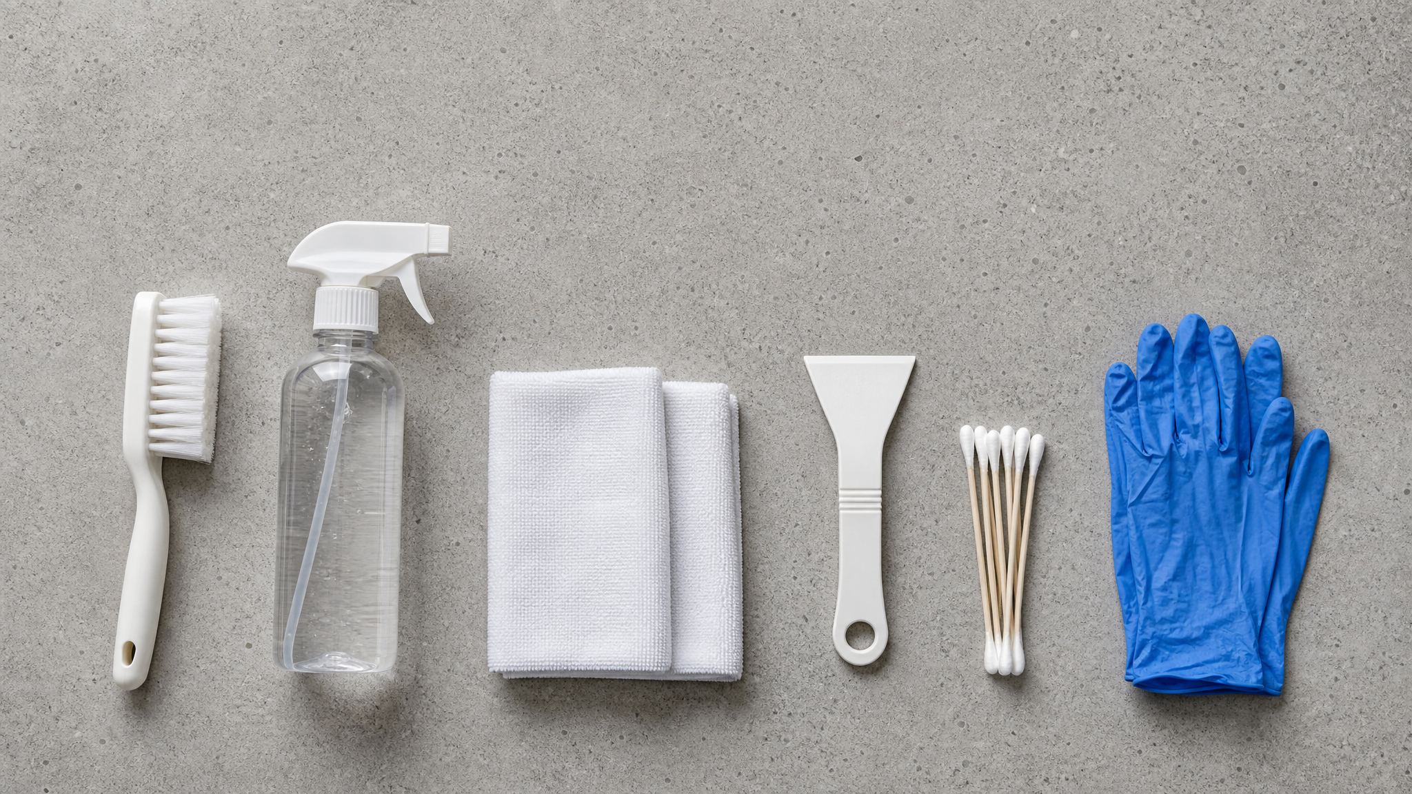 Flat lay of a sealant joint cleaning kit: soft brush, spray bottle, microfiber cloths, scraper and nitrile gloves